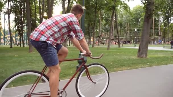 Seguir a joven hombre guapo montando una bicicleta vintage al aire libre. Un tipo deportivo en bicicleta en el parque. Vida activa saludable. Vista lateral Cerrar cámara lenta — Vídeo de stock