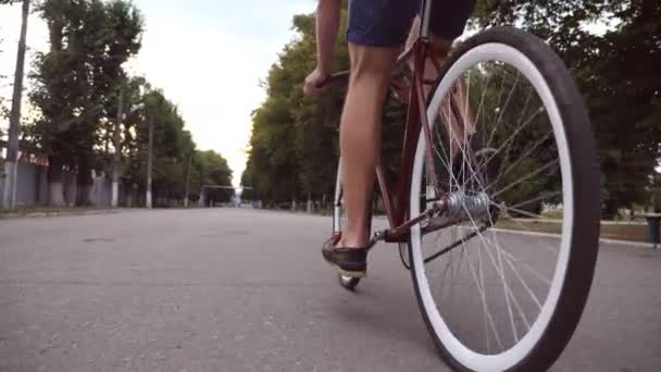 Jovem andando de bicicleta vintage na estrada do parque. Um tipo desportivo a andar de bicicleta ao ar livre. Estilo de vida ativo saudável. Ângulo de visão baixo Fechar Movimento lento — Vídeo de Stock