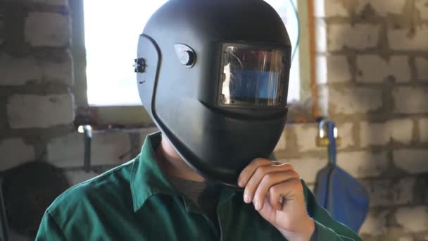 Soldador abre la máscara y mirando a la cámara. Retrato de un hombre guapo con barba trabajando en su garaje o taller. Cámara lenta Primer plano — Vídeos de Stock