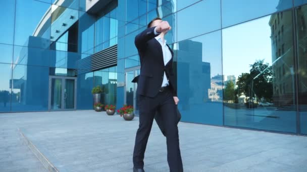 Ein junger, fröhlicher Geschäftsmann im Anzug tanzt auf der Straße und feiert seine Leistung. Erfolgreicher Büroangestellter mit Aktentasche beim Siegestanz in der Nähe moderner Gebäude. Erfolgskonzept. Zeitlupe — Stockvideo