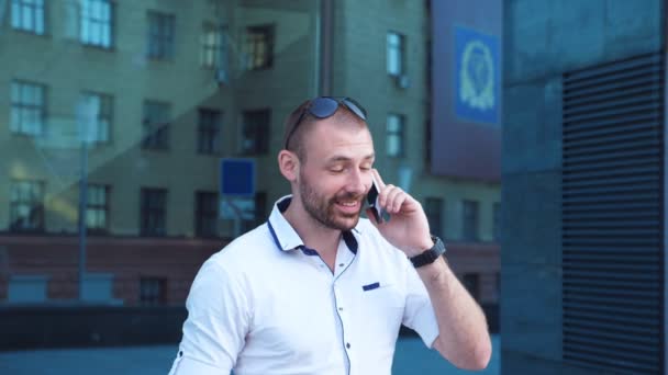 Hombre de negocios guapo hablando por teléfono cerca de la oficina y tener emociones positivas. Joven hombre de negocios escuchó buenas noticias en el teléfono celular y se alegra al aire libre. Guy está contento con la conversación. Lento mo Primer plano — Vídeos de Stock