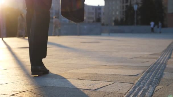 Pés de homem de negócios com pasta andando na rua da cidade ao pôr-do-sol. Empresário a viajar para o trabalho. Um tipo confiante a caminho do escritório. Trabalhador a ir ao ar livre. Visão traseira para trás Close up — Vídeo de Stock