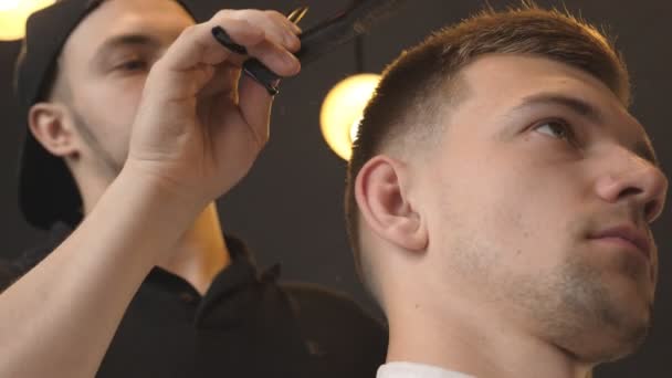 Perfil de un peluquero profesional peinando el cabello de un joven en el salón. Un tipo guapo arreglándose el pelo en la barbería de moda. Proceso de peinado. Vista lateral Cerrar cámara lenta — Vídeos de Stock