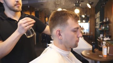 Genç Kuaför berber dükkanı kesme sonra erkek saç spreyi üzerinde su püskürtme. Kuaför saç onun müşterinin salonda tarama. Saç şekillendirme işlemi. Ağır çekim Dolly atış kapatın