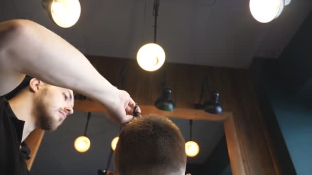 Dolly tiro de peluquero masculino peinando el pelo de su cliente en la barbería de moda. Vista trasera de un joven vistiéndose el pelo en el salón. Proceso de peinado. Primer plano: cámara lenta — Vídeo de stock