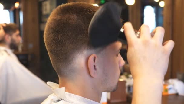 Peluquero masculino usando un talco para clientes jóvenes en el salón. Peluquería utiliza cepillo para limpiar chico de pelo cortado en la barbería. Peluquero haciendo procedimientos cosméticos al cliente. Vista lateral Cerrar cámara lenta — Vídeos de Stock