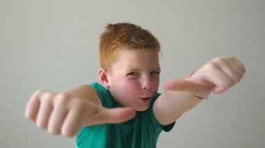 Sevimli bebek başarısını kutluyor ve baş parmağını kaldırıyor. Yüzünde neşe ifadesi olan erkek çocuğun duygularını kapat. Kapalı alanda çilleri olan kızıl saçlı yakışıklı çocuğun portresi. Yavaş çekim