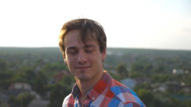 Cityscape arka plan, çatıda oturan genç mutlu adam portresi. Yüzünde sevinç ifadesi ile kameraya bakarak gülümseyen yakışıklı olan. Mutlu bir insan samimi duyguların. Kadar yakın çekim dolly