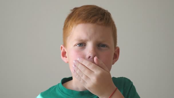 Le gamin couvre sa bouche d'une main qui lui fait un choc et un étonnement sur le visage. Adorable enfant regarde dans la caméra avec plaisir et surprise au visage. Portrait d'un beau jeune garçon. Ralenti Fermer — Video