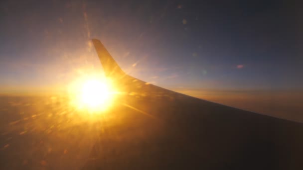 Uçak penceresinden güneşin doğuşuna ya da batışına bak. Bulutların üzerinde güneş ışığıyla uçan uçağın kanatları. Gökyüzünde uçak uçuşu. Hava yoluyla seyahat etme kavramı. Güzel bir geçmişi olan bir uçakla seyahat. — Stok video