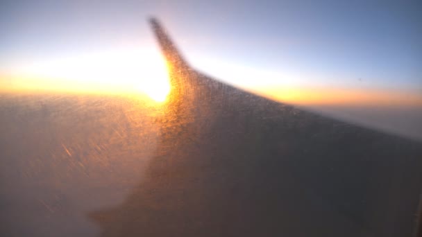Vervagen uitzicht van vliegtuigraam naar zonsopgang of zonsondergang. Silhouet van de vleugel van het vliegtuig vliegen boven de wolken met zon licht. Vliegtuig vlucht bij Sky. Concept van reizen door de lucht. Defocus geschoten — Stockvideo