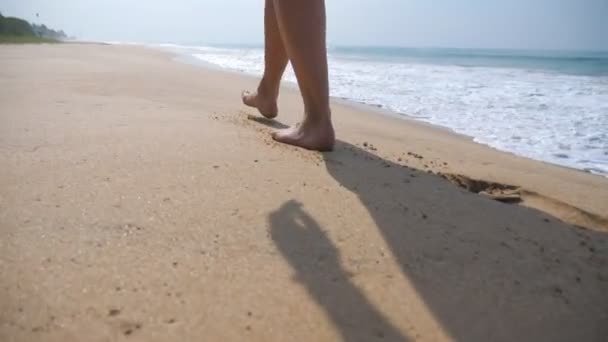 Piedi femminili che camminano sulla sabbia dorata sulla spiaggia con onde oceaniche sullo sfondo. Gambe di giovane donna che calpesta la sabbia. Ragazza scalza sulla riva del mare. Vacanze estive. Rallentatore Close up — Video Stock