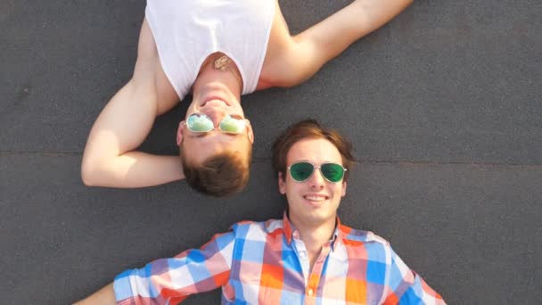 Bovenaanzicht van twee knappe jongens in zonnebril liegen met geluk en vreugde uitdrukking op het gezicht. Gelukkig jongemannen rusten en genieten van het leven samen. Vrienden buiten ontspannen. Slow motion close-up — Stockvideo