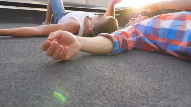 Deux jeunes gays couchés sur le toit et fumant avec un soleil éclatant à l'arrière-plan. Des hommes se reposant et profitant de la vie ensemble. Amis se détendre en plein air au coucher du soleil. Belle vue du bas Lent mo Gros plan — Video