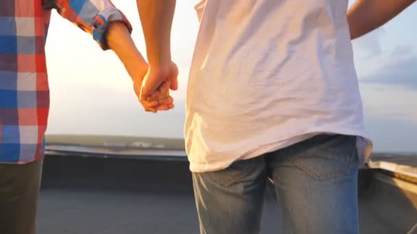 Друзья во время бега держатся за руки и радуются жизни с прекрасным закатом на заднем плане. Неузнаваемая гей-пара показывает радость и счастье на открытом воздухе. Молодые люди проводят время вместе — стоковое видео