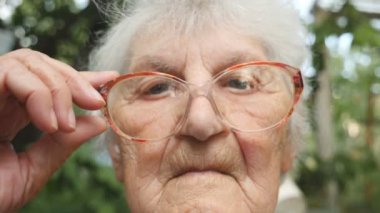 Yaşlı kadın gözlüklerini düzeltiyor ve kameraya bakıyor. Büyükanne açık portresi. Yavaş hareket kapatmak