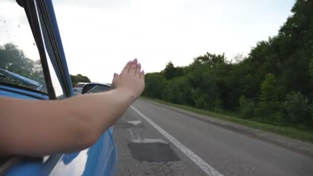 Brazo femenino fuera del coche retro jugando con el viento durante el viaje de verano. Mujer joven saludando con su mano en el viento en el viaje. Chica pone su brazo por la ventana del coche viejo para sentir la brisa. Movimiento lento — Vídeos de Stock