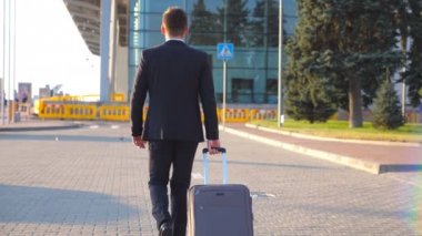 Tanımlanamayan genç iş adamının gün batımında havaalanı terminaline yürüyüp bavulunu tekerleklerle çekişi. Başarılı bir erkek iş adamı valiziyle şehir caddesine çıkıyor. Kapat.