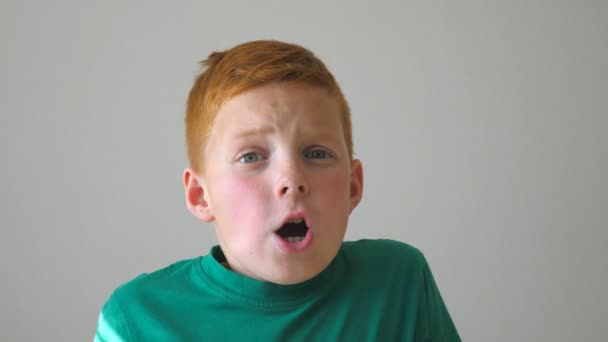 Close up of adorable red-haired boy grabbing his head and showing joy on his face. Hahdsome kid rejoicing achievement and giving a thumbs up. Portrait of happy boy with freckles indoor. Slow motion — Stock Video