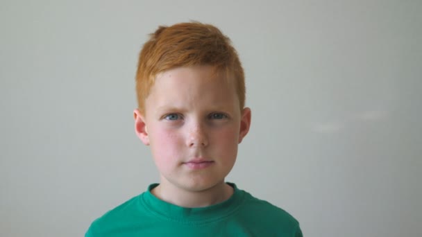 Portrait of young serious red-haired boy with freckles inside. Adorable handsome kid looking into camera indoor. Close up emotions of little male child with sad expression on face. Slow motion — Stock Video