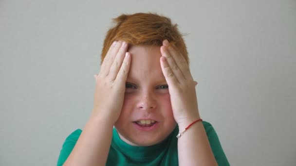 Retrato de un niño joven y feliz agarrando su cabeza y mostrando alegría en su cara por dentro. Guapo chico pelirrojo con pecas mirando a la cámara y levantar las manos regocijando logro. Movimiento lento — Vídeo de stock