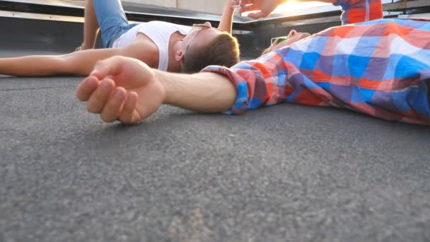 Young man lying with his boyfriend on roof and giving a cigarette to him. Handsome male couple spending time on rooftop of high-rise building and smoking together. Low angle view Close up — Stock Video