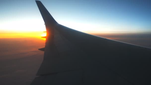 View from airplane window to sunrise or sunset. Wing of plane flying above the clouds with sun light. Aircraft flight at sky. Concept of traveling by air. Trip by airliner with beautiful background — Stock Video