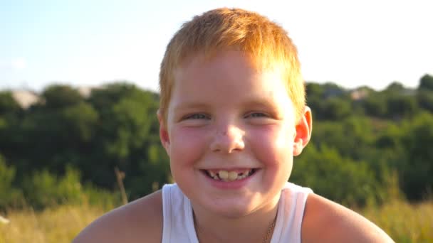 Portret szczęśliwego rudego chłopca z piegami śmieje się na zewnątrz. Urocze, przystojne dziecko patrzące w kamerę z radosnym uśmiechem. Zbliż emocje męskiego dziecka z dobrą miną. Zwolniony ruch — Wideo stockowe