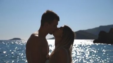 Arka plan, su yüzeyinde güneş ışık yansıması ile Sahil yakınındaki öpüşme güzel çiftinin yakın çekim. Genç çift yaz tadını güneşli günde seyahat. Sevgi ve mutluluk kavramı