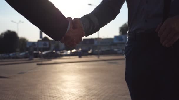 I colleghi giovani che si incontrano e stringono la mano a strada di città su tramonto. Stringi la mano all'aperto. Crane girato di due uomini d'affari che si salutano sullo sfondo del parcheggio auto. Rallentatore — Video Stock