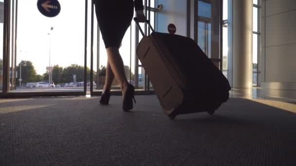 Geschäftsfrau verlässt Flughafen durch automatische Glastür mit ihrem Gepäck. junge Frau in High Heels, die vom Terminal geht und Koffer auf Rädern rollt. Konzept der Arbeitsreise oder Reise. Zeitlupe — Stockvideo