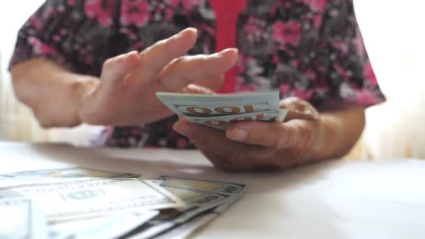 Abuela sosteniendo un paquete de dinero en las manos y tirando billetes de cien dólares sobre la mesa. Brazos de anciana esparciendo moneda extranjera en el escritorio frente a la cámara. Primer plano: cámara lenta — Vídeos de Stock