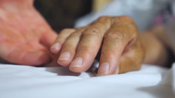 Young man holding and gentle touching hand of sick mature woman in hospital. Grandson comforting wrinkled arm of his old grandmother in medical clinic. Caring and loving concept. Close up Slow motion — Stock Video