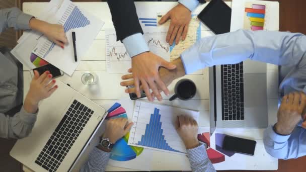 Vista dall'alto a mani di quattro uomini d'affari che festeggiano il raggiungimento. Gruppo di datori di lavoro impilato le braccia uno per uno in unità mostrando gioioso. Team creativo che lavora in un ufficio moderno. Concetto di successo — Video Stock