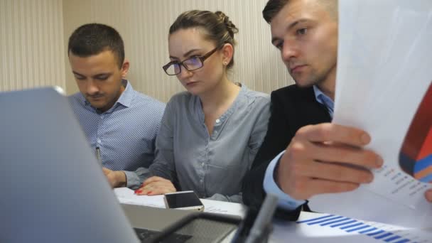 Grupo de jóvenes empresarios sentados a la mesa en una oficina moderna y trabajando en un nuevo proyecto. Colegas revisan cuidadosamente los documentosdurante el proceso de trabajo. Trabajadores de oficina ocupados desarrollando negocios — Vídeo de stock