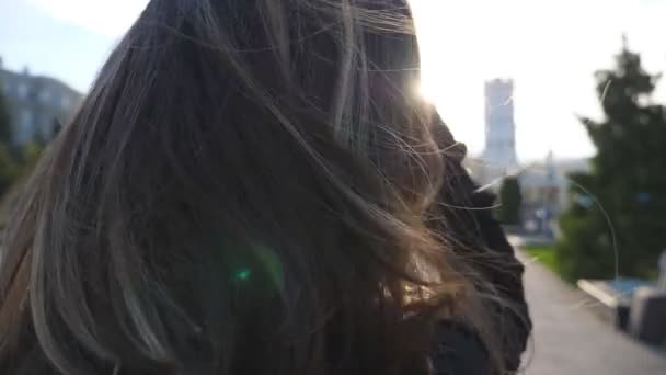 Oigenkännliga mörkhåriga kvinnan står på Urban Street och uträtning hår. Flicka som står på stads miljö med starkt solljus i bakgrunden. Lady njuter av bris leker med hennes hår — Stockvideo