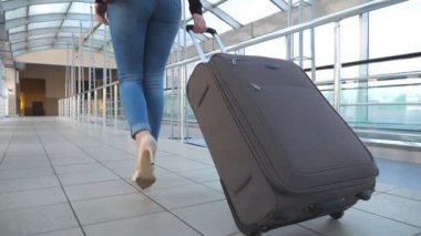 İş kadınının bacakları bavuluyla terminal koridorundan geçiyor. Yüksek topuklu ayakkabılı, tekerlekli bavulu yuvarlayan tanınmamış bir kız. Bayan seyahate çıkıyor. Seyahat konsepti. Yavaş çekim. Yakın çekim.