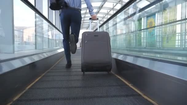 ターミナルのホールで実行し、車輪の上のスーツケースを引いて成功したビジネスマンの足。彼の荷物を持った若い男にカメラ フォローはフライトに遅刻です。男はビジネスの旅を急ぐ。スローモーション — ストック動画
