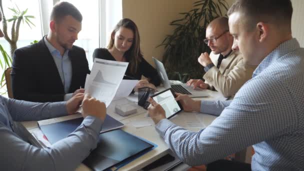 Ομάδα νέων επιχειρηματιών που κάθονται στο τραπέζι του σύγχρονου γραφείου και εργάζονται σε ένα νέο έργο. Οι συνάδελφοι εξετάζουν προσεκτικά τα έγγραφα κατά τη διαδικασία εργασίας. Οι υπάλληλοι του γραφείου ασχολούνται με την ανάπτυξη επιχειρήσεων. Αργή κίνηση — Αρχείο Βίντεο