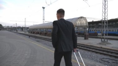 Tren istasyonunda yürüyüş ve tekerlekler üzerinde bavul çekerek uygun tanınmaz başarılı işadamı. Kamera iş gezisi gidiyor onun bagaj ile genç adam izleyin. Yavaş hareket geri görünümü