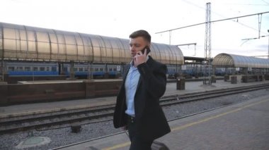 Onun bagajları ile tren istasyonunda yürümek ve telefonda konuşurken yakışıklı işadamı. Demiryolu yakınlarında gezinirken ve iş görüşmesi yapan genç bir iş adamı. İş gezisi kavramı. Yavaş Mo