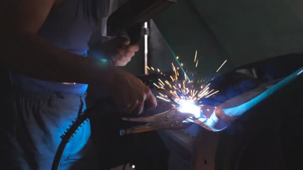 Mano masculina del reparador profesional o del trabajador mecánico suelda las piezas metálicas del coche viejo usando la máquina de soldadura en taller. Los destellos y chispas vuelan desde el trabajo de soldadura en la oscuridad en el garaje. Vista lateral Primer plano — Vídeos de Stock