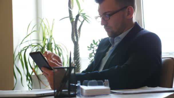 Gutaussehender Geschäftsmann mit Brille, der im Büro statistische Daten auf einem Tablet-PC analysiert. Jungunternehmer gibt Anweisungen für männliche Arbeiter. Konzept des Business Lifestyles. Zeitlupe — Stockvideo