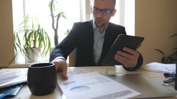 Seriös affärsman i glasögon tittar på diagram med statistik om papper medan du arbetar på digital enhet. Framgångsrik entreprenör som analyserar statistisk data information på en Tablet PC i Office — Stockvideo