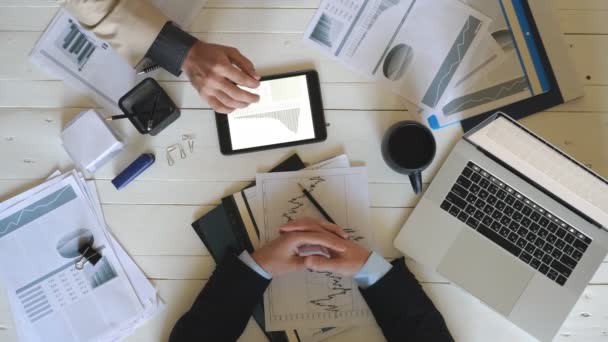 Vista dall'alto mani maschili di due colleghi che controllano i grafici con le statistiche e discutono le relazioni finanziarie in carica. Uomini d'affari di successo seduti al tavolo di legno e lo sviluppo di un nuovo progetto di business — Video Stock