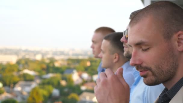 Faces of confidence businessmen looking at cityscape from balcony and enjoys beautiful view. Profile of young entrepreneurs watching panorama of the city from terrace of high-rise building. Side view — Stock Video