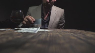 Erkek bağımlı, kredi kartıyla kokain yapıyor ve telefon ekranından banknot la uyuşturucu kokluyor. Uyuşturucu satıcısı burnunu 100 dolarlık banknota silerek camdan brendi içiyor