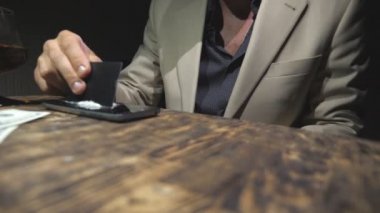 Kredi kartı tutan ve akıllı telefondan kokain üreten bağımlıların erkek elini kapat. Uyuşturucu satıcısı telefon ekranından 100 dolarlık banknotlar yollamış. Düşük açı görünümü