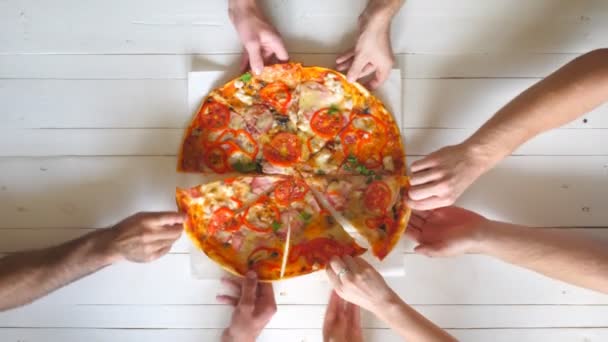 Top view męskie i żeńskie ręce biorąc plastry pizzy z serem, pomidorami i szynką z dostaw żywności. Grupa głodnych przyjaciół siedzi przy biurku i dzieli się pysznym obiadem na drewnianym tle stołu — Wideo stockowe