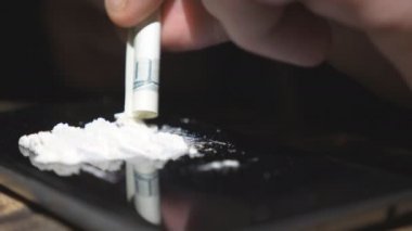 Bağımlının erkek elini tutup yüz dolarlık banknotu tutup telefon ekranından kokain ivediliği. Bağımlılık ve madde bağımlılığı kavramı. Düşük açı görünümü Yavaş çekim